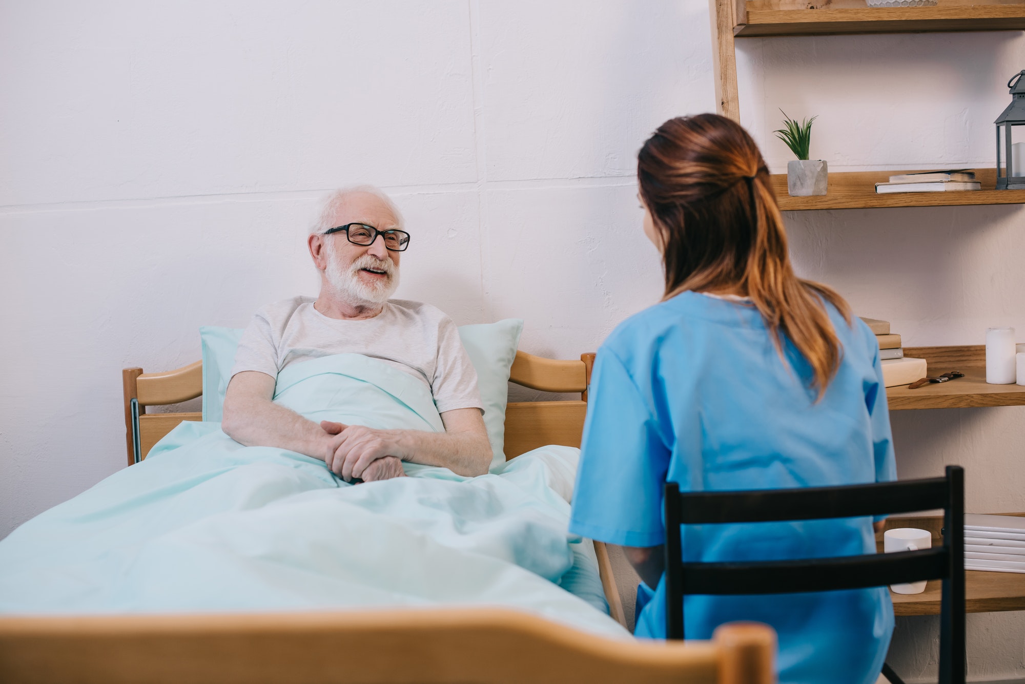 Smiling old patient in bed talking to nurse